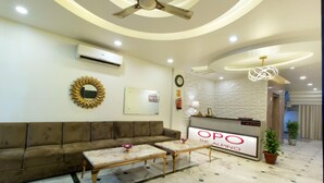 A reception area with a sofa, two coffee tables, a reception desk, a clock, and a ceiling fan. - OPO Collection Alpino (New Delhi)