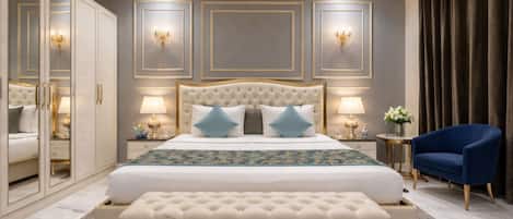 A bedroom with a large bed, bedside lamps, a chandelier, a blue armchair, and a mirror cabinet.