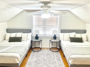 Ein Schlafzimmer mit zwei Betten, einem Deckenventilator, einem Fenster mit Jalousien und einem kleinen Teppich.
