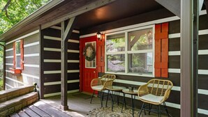 A wooden porch with a red door, two wicker chairs, and a small table. - Secluded Cabin w/ Hot Tub & Stunning Mountain (Sevierville)