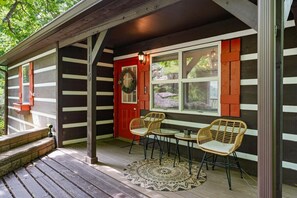 A wooden porch with a red door, two wicker chairs, and a small table. - Secluded Cabin w/ Hot Tub & Stunning Mountain (Sevierville)