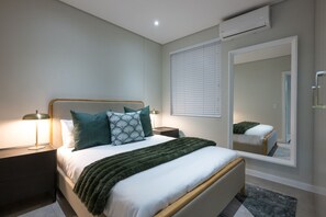 A modern bedroom with a bed, bedside tables, a mirror, and an air conditioning unit. - Slick Garden Gem 300 on Florida RD (Morningside, KwaZulu-Natal)