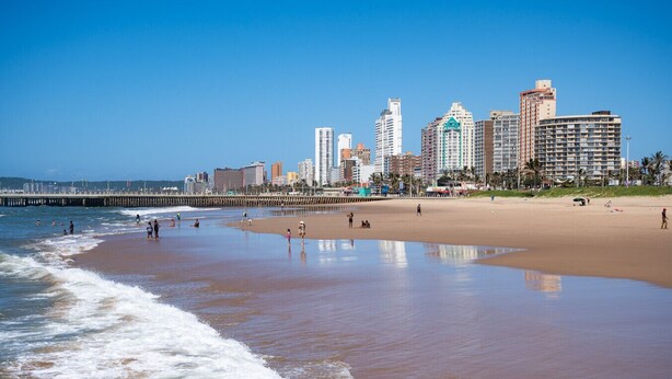 Una playa con olas, un muelle y un horizonte urbano con edificios altos.