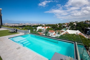 Ein Pool auf dem Dach mit Blick auf die Stadt, eine Rasenfläche und eine Liege.