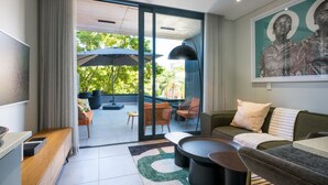 Una sala moderna con sofá, mesa de centro y sillones, puerta corrediza de vidrio que da a un patio exterior con sombrillas y asientos.
