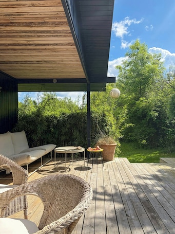 A wooden deck with a covered seating area, a round table, and a potted plant.. Classic 70s house by beach in Smidstrup