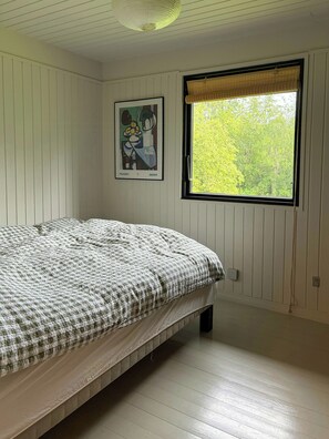 Une chambre Ă coucher avec un lit, une fenĂȘtre donnant sur des arbres et une Ćuvre dâart encadrĂ©e accrochĂ©e au mur.