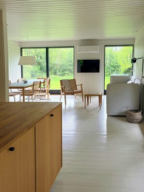 Un salon moderne avec une table à manger en bois, deux chaises en bois, un canapé et un téléviseur fixé au mur.