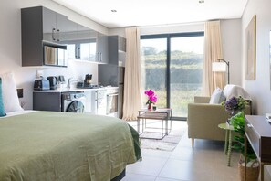 Ein modernes Hotelzimmer mit einem großen Bett, einer Küchenzeile, einem Essbereich und einem Balkon mit Blick.