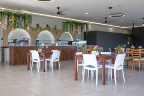 Ein modernes Restaurant mit einer Holztresen, weißen Stühlen, hängenden Pflanzen und Pendelleuchten.