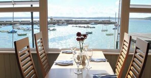 Una mesa de comedor con sillas y un florero, con vistas a un puerto deportivo y barcos.