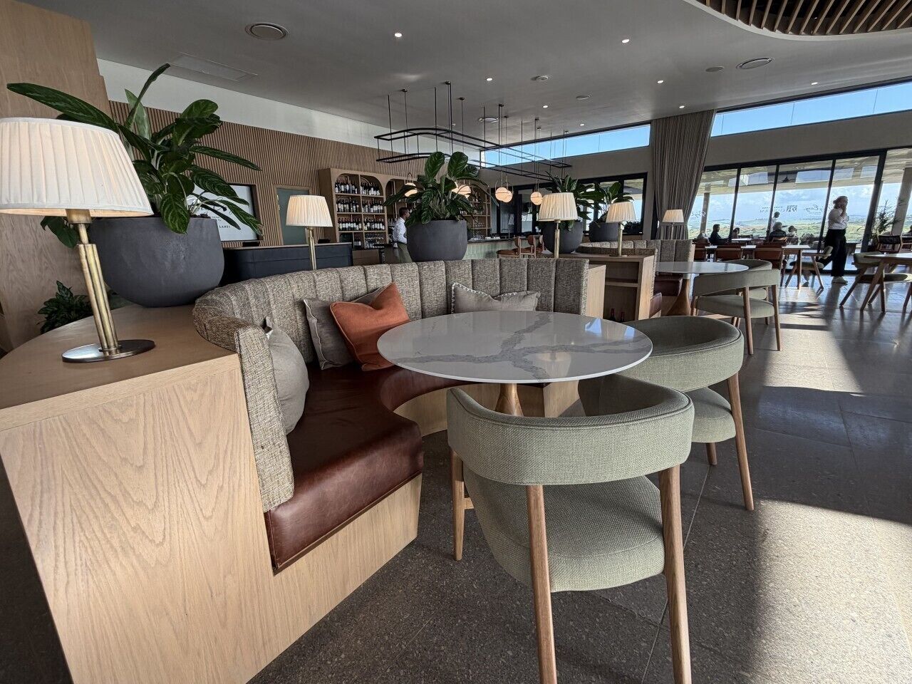 A modern lounge area with a sofa, round tables, and potted plants.