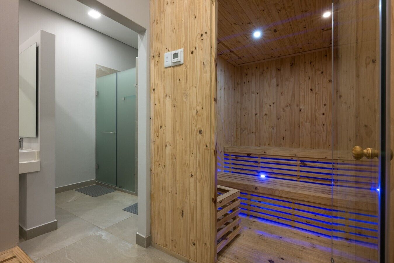 Een sauna met houten wanden en een glazen deur, een wit wastafelmeubel en een douchehoek.