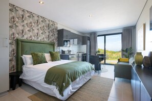 A modern bedroom with a large bed, a kitchen area, and a view of the landscape. - Sleek Coastal Studio in Zimbali OC H26 (Ballito, KwaZulu-Natal)