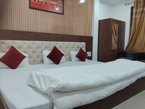 A hotel room with a large bed, a headboard, a wardrobe, and a painting on the wall. - Shree Ram Seva Bhakt Niwas (Ayodhya)