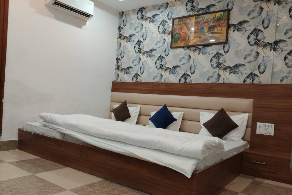 Una cama individual con cabecera de madera, un aire acondicionado de pared y un papel tapiz estampado con un cuadro enmarcado encima.