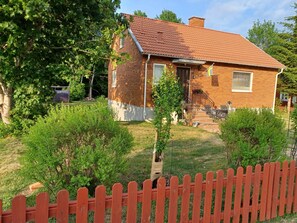 A two-story house with a red-tiled roof, a brick exterior, and a small front yard with a wooden fence. - Cosy HAPPY PLACE Experience the kingdom of Crystal in the Swedish Smaland. (Boda glasbruk)
