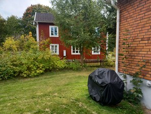 Une maison en briques rouges avec une cour clôturée, un objet abrité et un arbre.