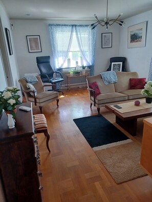 A living room with a sofa, chairs, a coffee table, a radiator, and a window with curtains. - Cosy HAPPY PLACE Experience the kingdom of Crystal in the Swedish Smaland. (Boda glasbruk)