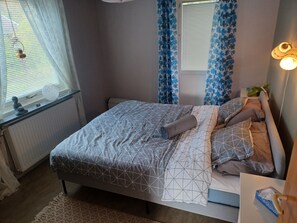 A neatly arranged bedroom with a bed, bedside table, and a window with curtains. - Cosy HAPPY PLACE Experience the kingdom of Crystal in the Swedish Smaland. (Boda glasbruk)