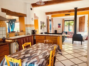 Une cuisine avec un coin repas, des poutres en bois, une grande fenêtre et une vue sur l’extérieur.