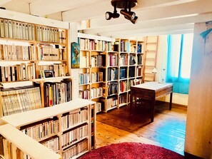 A room with wooden bookshelves filled with books, a wooden desk, and a red rug. - The Cocon Lou Jaïa (Corbère)