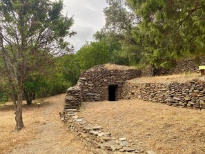 A stone structure with a doorway, surrounded by dry grass and trees. - The Cocon Lou Jaïa (Corbère)