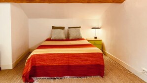 A bedroom with a bed, two pillows, a nightstand with a lamp, and exposed wooden beams on the ceiling. - The Cocon Lou Jaïa (Corbère)