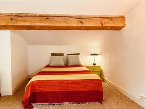 A bedroom with a bed, two pillows, a nightstand with a lamp, and exposed wooden beams on the ceiling. - The Cocon Lou Jaïa (Corbère)