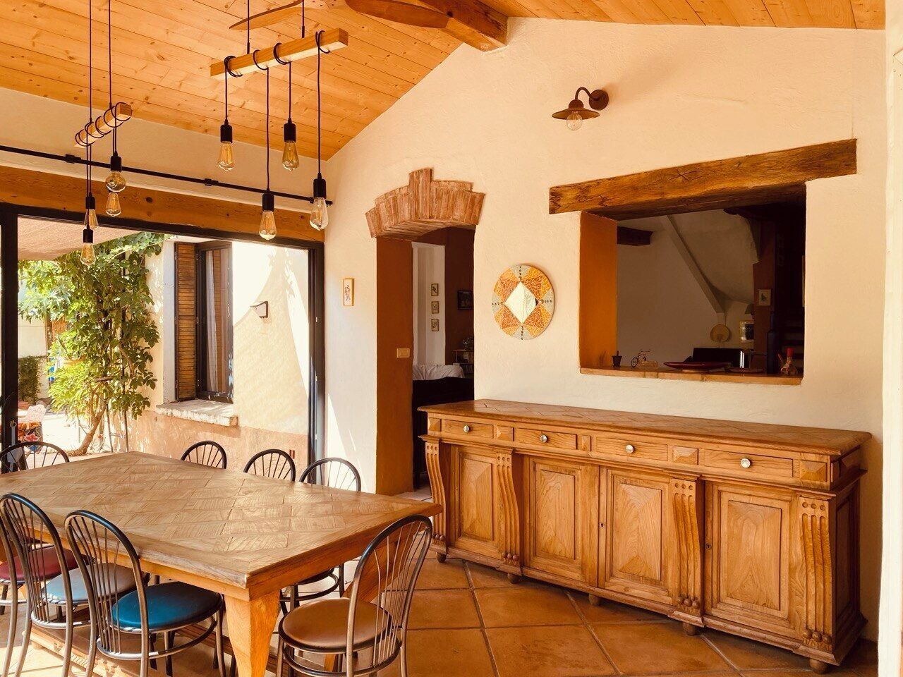 A dining area with a wooden table and chairs, a wooden cabinet, and pendant lighting.