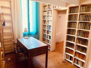 Une pièce comprenant un bureau en bois, une chaise, une lampe et une bibliothèque remplie de livres.