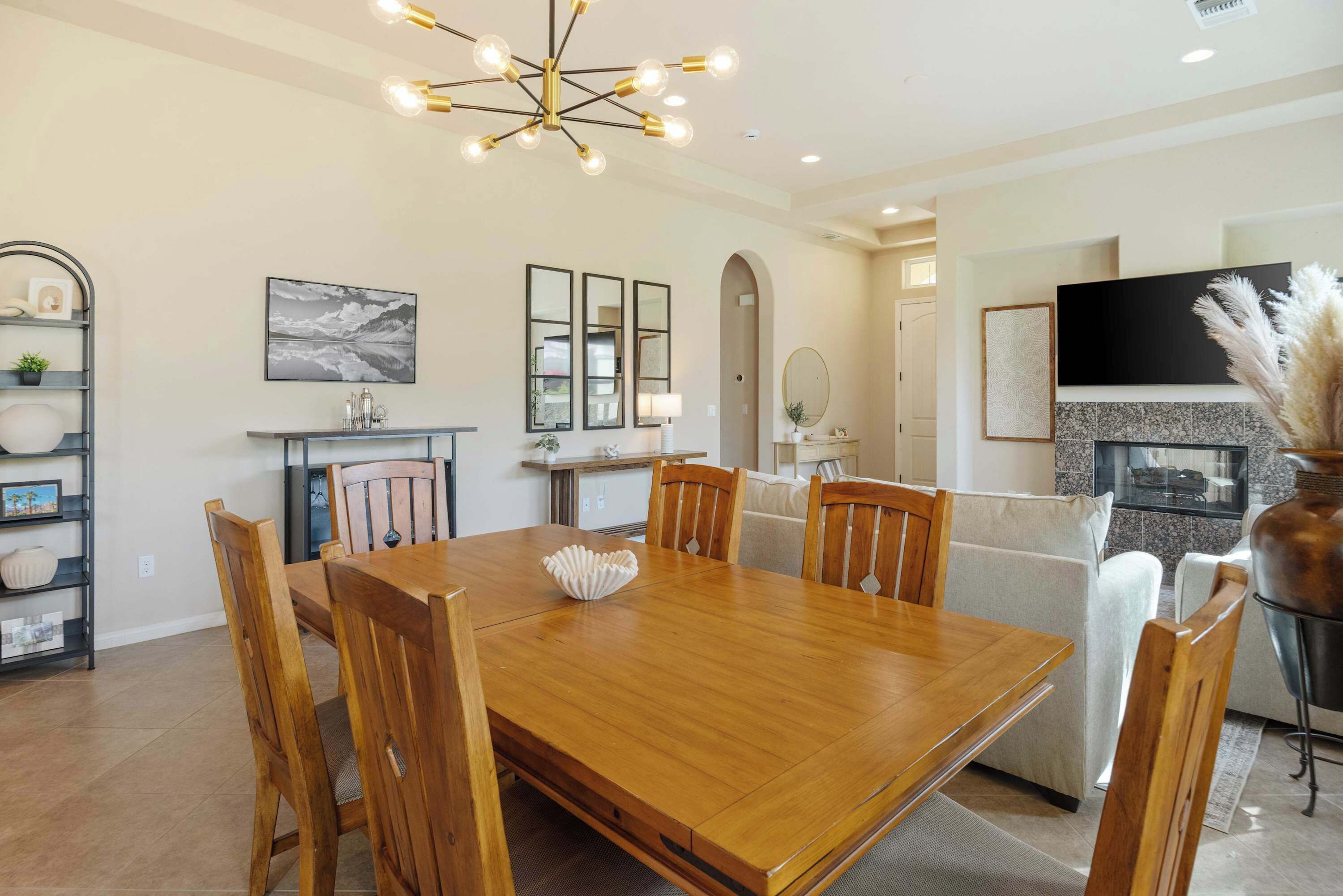 A dining area with a wooden table and chairs, a chandelier, and a fireplace.