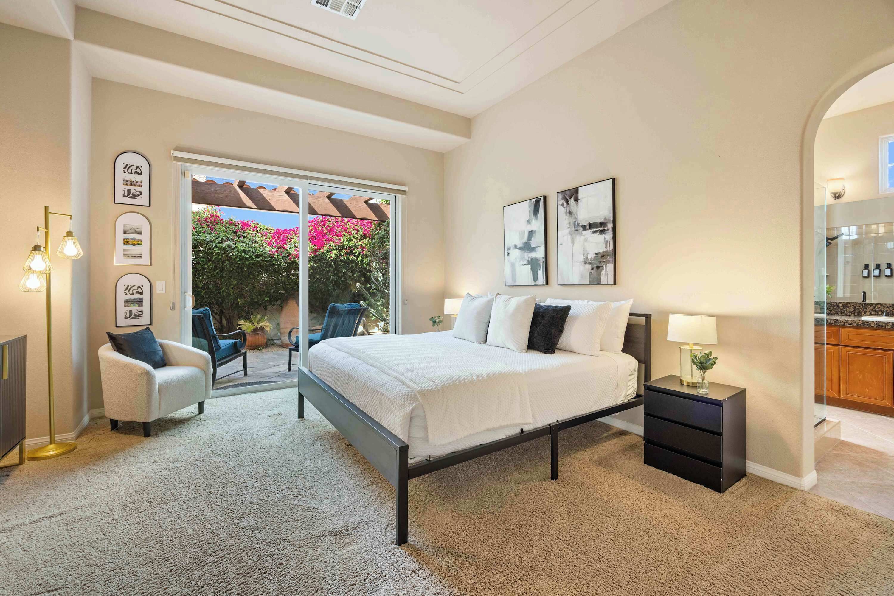Une chambre à coucher comprenant un lit, une table de chevet, une chaise et donnant sur un balcon agrémenté de plantes et doté d’une fenêtre.
