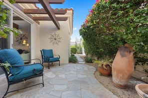 A patio with stone flooring, two blue cushioned chairs, a large terracotta pot, and a wall-mounted decorative piece. - Sky Villa Puerta Azul Retreat w Pools Gym (La Quinta)