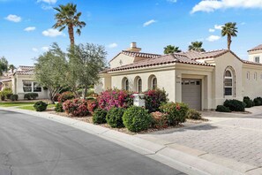 A residential house with a tiled roof, arched windows, and a front yard with various shrubs and a palm tree. - Sky Villa Puerta Azul Retreat w Pools Gym (La Quinta)