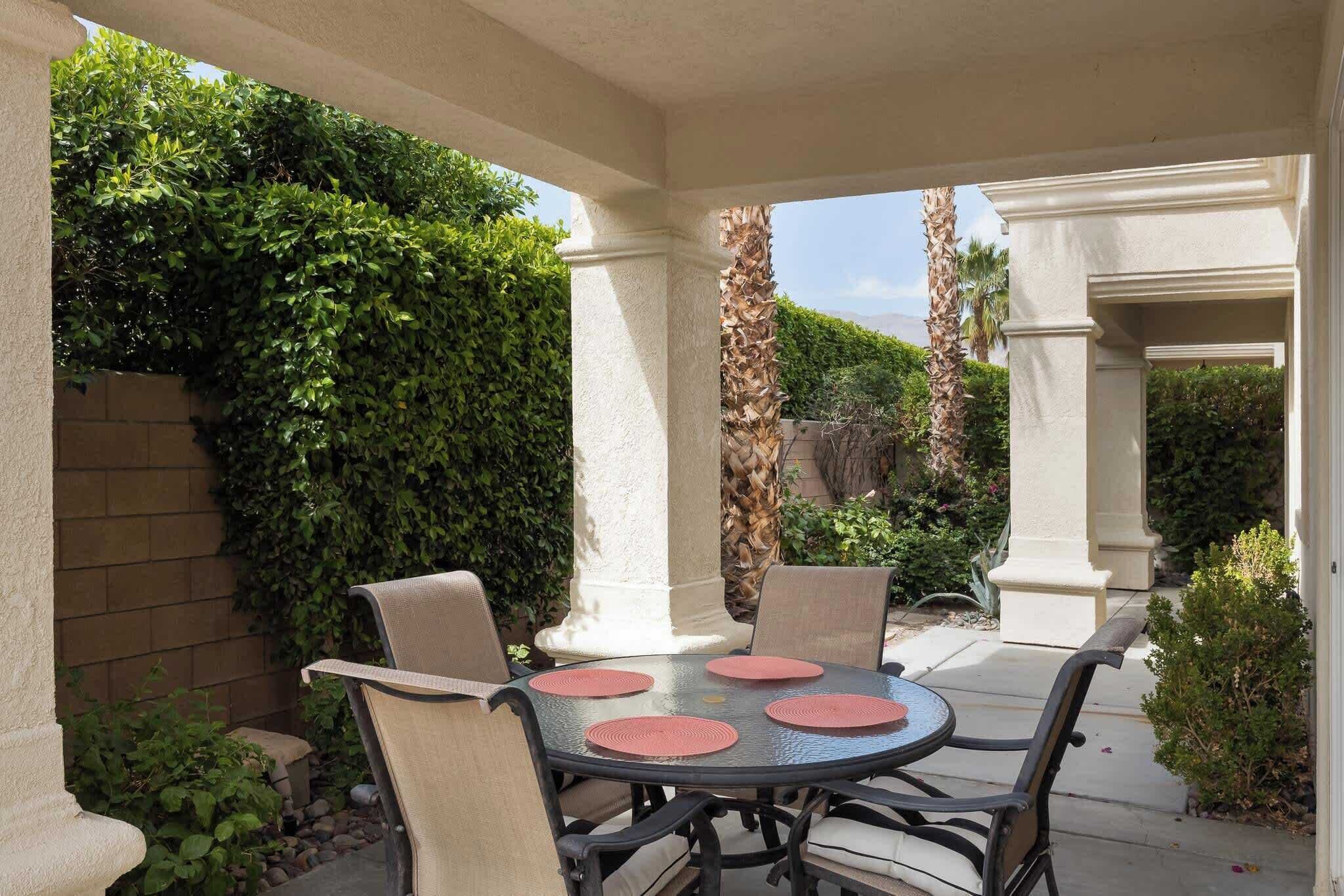An outdoor patio with a round table, four chairs, and a decorative wall of greenery.