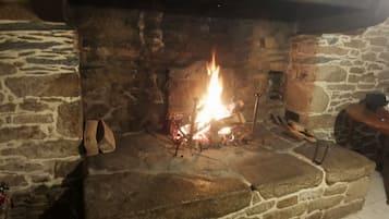 Una chimenea de piedra con fuego encendido, un banco de madera a la derecha y una pared de piedra.