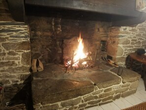Ein Steinkamin mit Feuer, eine Holzbank zur Rechten und eine Steinsäule.