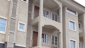 A multi-story building with balconies, a central entrance with a door, and a small garden area. - The Oliver Lofts Hotels (Abuja)