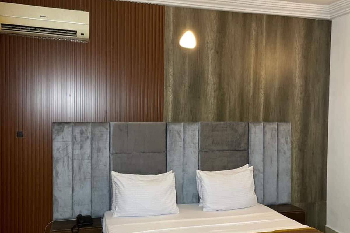 A hotel room with a large bed, two bedside tables, an air conditioning unit, and a wooden panel wall.