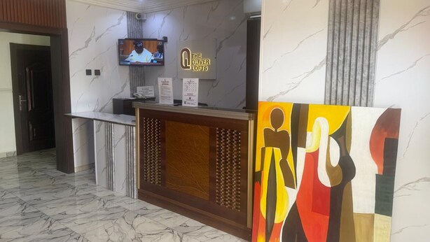 A reception desk with a television, a sign for 'The Oliver Lofts,' and a large abstract painting. - The Oliver Lofts Hotels (Abuja)