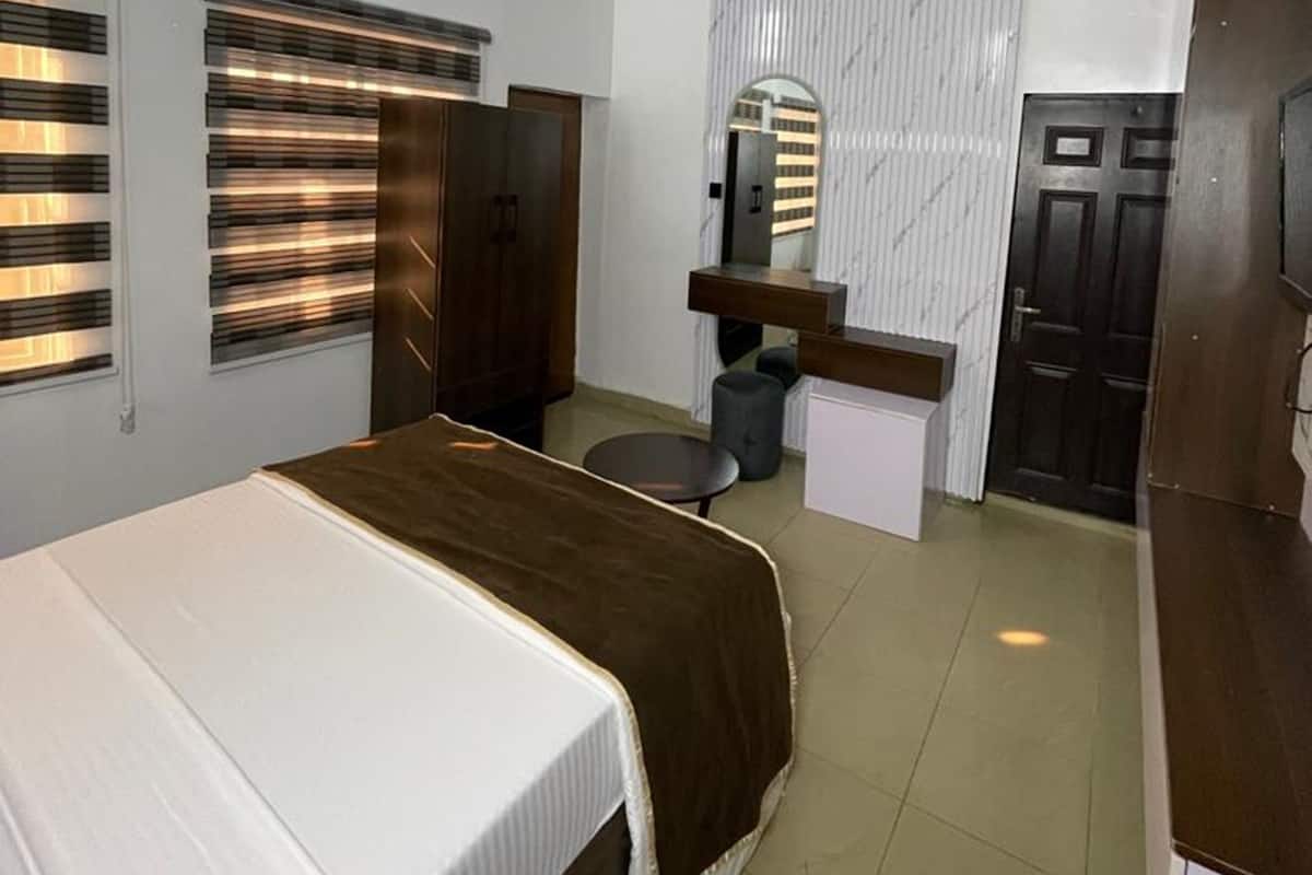 A hotel room with a bed, a desk, a mirror, a wardrobe, and a door.