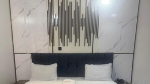 A modern hotel room with a large bed, a headboard with vertical lines, and a marble-patterned wall. - The Oliver Lofts Hotels (Abuja)