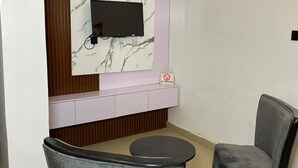 A modern room with a marble-patterned wall, a mounted TV, a 'No Smoking' sign, and two grey chairs. - The Oliver Lofts Hotels (Abuja)