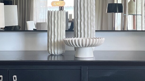 Ein modernes Interieur mit dunkler Holzbalkendecke, einer weißen Vase und einer dekorativen Schale auf einer Arbeitsplatte.