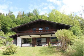 A wooden cabin with a large window, a balcony, and a garden area. - Chalet to feel good Golf, ski, mountains, lake (Goldegg)