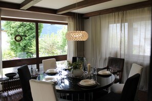 A dining area with a round table, chairs, a hanging light fixture, and a view of greenery outside. - Chalet to feel good Golf, ski, mountains, lake (Goldegg)