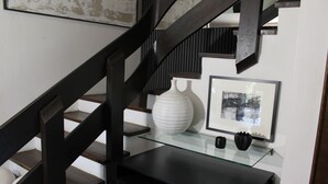 Eine Treppe mit dunklen Holellböcken, eine Glasablage mit einer weißen Vase und einem gerahmten Bild sowie ein schwarzer Schreibtisch.