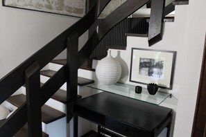 A staircase with dark wooden railings, a glass shelf with a white vase and a framed picture, and a black desk. - Chalet to feel good Golf, ski, mountains, lake (Goldegg)