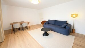 A modern living room with a blue sofa, a round coffee table, and a dining area with a wooden table and chairs. - Liboria vacation apartment Starnberg with balcony for 6 persons (Starnberg)